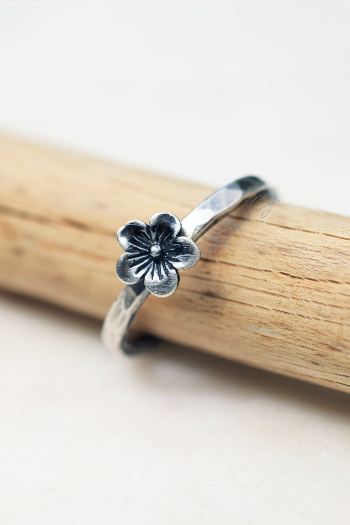 Silver flower ring on a wooden stick with a white background