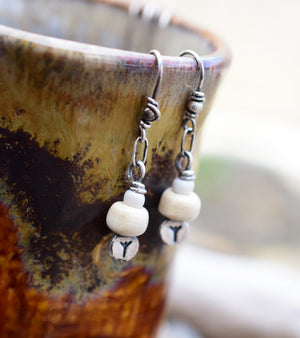 These earrings are built around Silver nugget headpins with the Algiz Rune. Handcrafted from .999 pure, raw silver and hand stamped with the tiny 3mm runes. Each one is unique and rustic in appearance.  Adorned with handcrafted porcelain beads in creamy off white, paired with rustic white African glass beads.  This little bead totem hangs from a small silver ring which attaches to the ear wires. This center ring gives the charms a nice movement.  The ear-wires are crafted from .925 sterling silver. Always. 