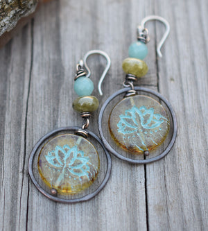 A pair of earrings made of gemstones and copper hoops with lotus flower beads and sterling silver ear wires on a wood background. 