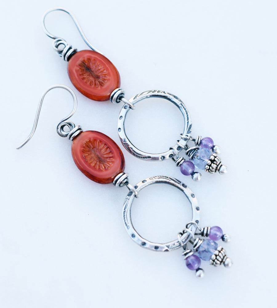 A pair of handcrafted silver hoop earrings with orange and amethyst beads.